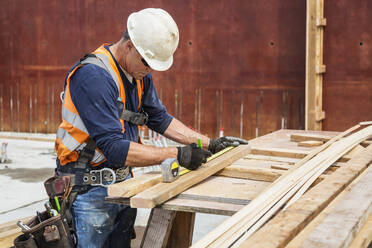 Kaukasischer Arbeiter misst Holz auf einer Baustelle - BLEF07647