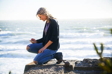 Caucasian girl using cell phone on hilltop overlooking ocean - BLEF07698