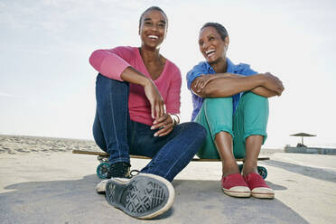 Ältere schwarze Frauen sitzen auf einem Skateboard am Strand - BLEF07753