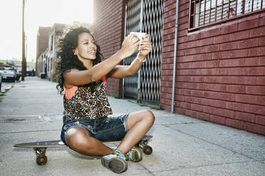 Hispanische Frau macht Handy-Foto auf Skateboard auf der Straße - BLEF07766