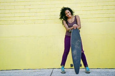 Hispanische Frau mit Skateboard auf einer Straße in der Stadt - BLEF07771