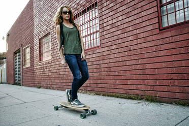 Gemischtrassige Frau fährt Skateboard auf einer Straße in der Stadt - BLEF07774