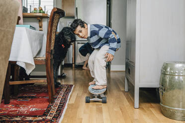 Mixed race boy riding skateboard in kitchen - BLEF07785