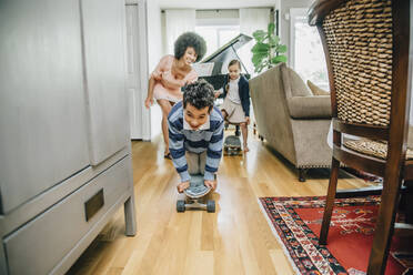 Gemischtrassige Familie beobachtet Junge beim Skateboardfahren im Wohnzimmer - BLEF07786