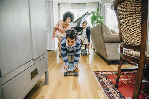 Mixed race family watching boy ride skateboard in living room - BLEF07786