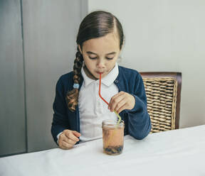 Gemischtrassiges Mädchen trinkt Saft aus einem Glas durch einen Strohhalm - BLEF07789