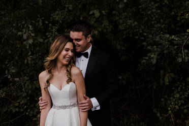 Glückliche junge Braut und Bräutigam lachend vor Laub - ISF21516