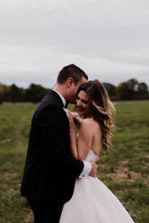 Romantic young bride and groom hugging in field - ISF21518
