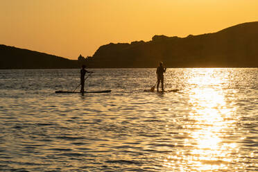 Mutter und Sohn beim Standup-Paddleboarding im Meer bei Sonnenuntergang, Limnos, Khios, Griechenland - ISF21519
