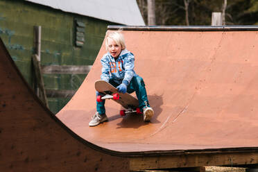 Junge, der sich auf einer hölzernen Skateboard-Rampe auf ein Skateboard setzt - ISF21551