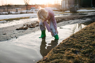 Boy rolling trousers up in rural meltwater puddle - ISF21557