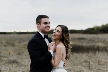 Glückliche junge Braut und Bräutigam umarmen und lachen im Feld - ISF21562
