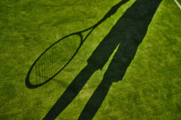 Abgeschnittener Schatten eines Tennisspielers mit Tennisschläger auf grünem Rasen - ISF21566