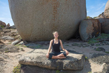 Junge Frau übt Lotus-Yoga-Pose auf Strandfelsen, Porträt, Kapstadt, Westkap, Südafrika - ISF21589