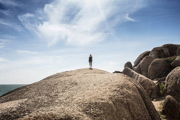 Young woman practicing yoga taking a break standing on top of beach boulder, Cape Town, Western Cape, South Africa - ISF21592