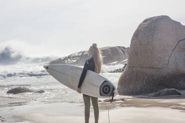 Junge Surferin mit Surfbrett, die vom Strand aus auf die Wellen schaut, Kapstadt, Westkap, Südafrika - ISF21602