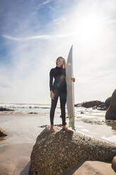 Junge Surferin mit Surfbrett am Strandfelsen, Porträt in voller Länge, Kapstadt, Westkap, Südafrika - ISF21639