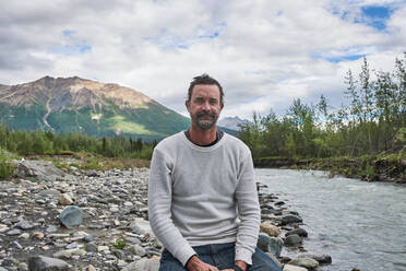 Mann entspannt sich am Bach, malerische Aussicht im Hintergrund, Chitina, Alaska, Vereinigte Staaten - ISF21651