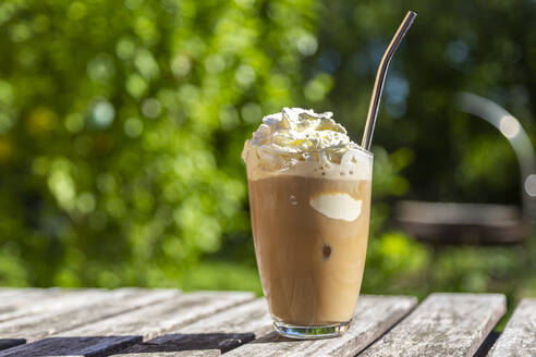 Ein Glas Eiskaffee mit Sahnehäubchen auf dem Gartentisch - SARF04313