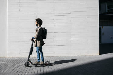 Man with backpack standing on E-Scooter - JRFF03335