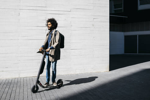 Mann mit Rucksack auf E-Scooter stehend - JRFF03336