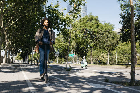 Man with backpack riding his E-Scooter on a bicycle lane - JRFF03343