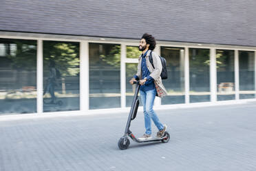 Mann mit Rucksack fährt schnell mit seinem E-Scooter in der Stadt - JRFF03345