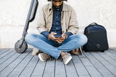 Mann sitzt auf seinem E-Scooter und benutzt ein Mobiltelefon - JRFF03349
