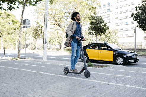 Mann mit Rucksack fährt mit seinem E-Scooter auf einem Fahrradweg - JRFF03355