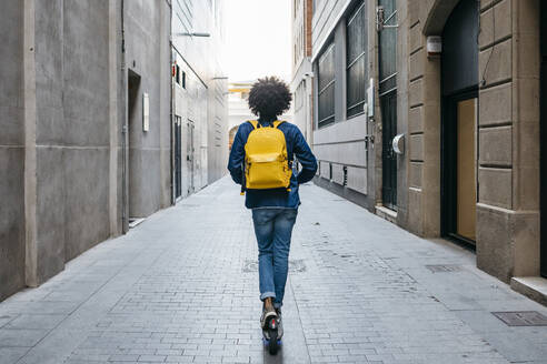 Back view of young man with yellow backpack on E-Scooter in the city, Barcelona, Spain - JRFF03359