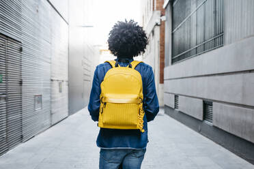 Rückenansicht eines jungen Mannes mit gelbem Rucksack auf einem E-Scooter in der Stadt - JRFF03361