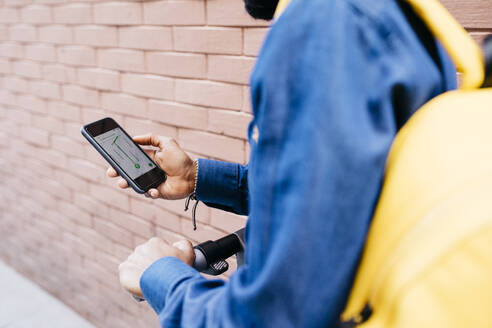 Mann mit Rucksack und E-Scooter bei der Nutzung einer Navigations-App auf seinem Mobiltelefon, Teilansicht - JRFF03369