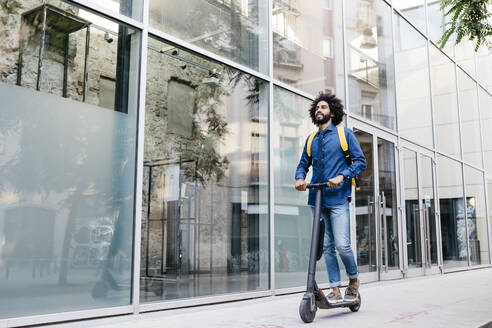 Man with backpack riding fast with his E-Scooter on pavement - JRFF03373