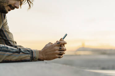 Tattooed man leaning on a wall during sunset using mobile phone, Barcelona, Spain - AFVF03328