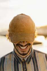 Laughing man wearing baseball cap at sunset - AFVF03340