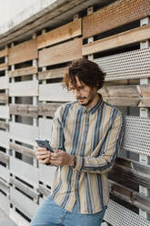 Man wearing striped shirt using smartphone - AFVF03358