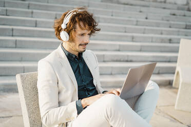 Businessman with headphones working on laptop outdoors - AFVF03379