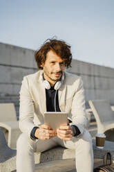 Portrait of businessman with headphones and digital tablet outdoors - AFVF03384