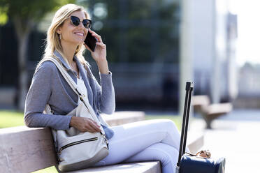 Junge Geschäftsfrau, die auf einer Bank sitzend mit einem Mobiltelefon spricht - JSRF00289