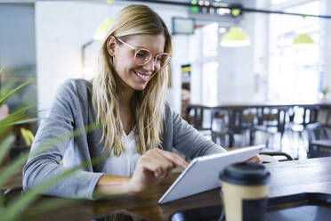 Junge Frau, die ihr digitales Tablet benutzt, während sie in einem Café Kaffee trinkt - JSRF00293