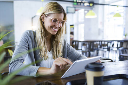 Young woman using her digital tablet while drinking coffee in the coffee shop - JSRF00293