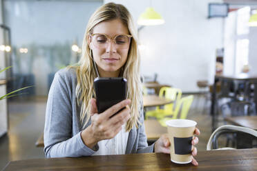 Junge Frau, die mit ihrem Mobiltelefon SMS schreibt, während sie im Café Kaffee trinkt - JSRF00295