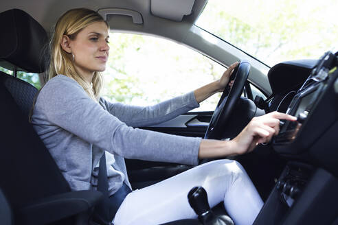 Young woman driver choosing a radio channel in her car - JSRF00308