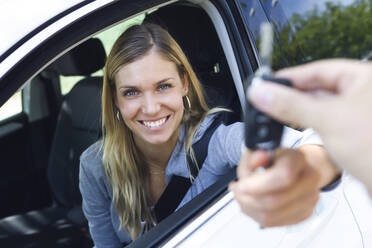 Portrait of smiling young woman looking at camera while holding car keys and give it to someone through the window - JSRF00312