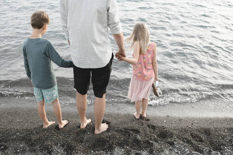 Rückenansicht eines Mannes, der Hand in Hand mit seiner kleinen Tochter und seinem Sohn an der Strandpromenade steht, lizenzfreies Stockfoto