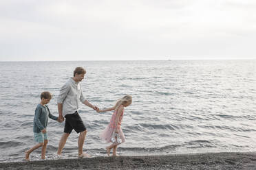 Father walking hand in hand with little daughter and son at seafront - EYAF00255