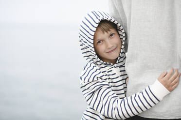 Portrait of smiling boy wearing striped hooded jacket hugging his father - EYAF00258