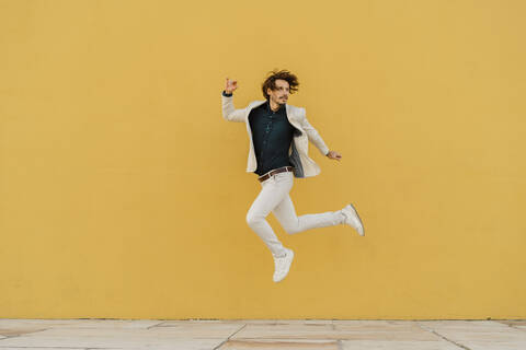 Geschäftsmann, der vor einer gelben Wand in die Luft springt, lizenzfreies Stockfoto