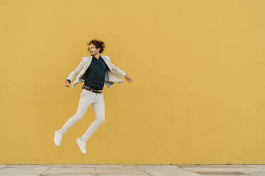 Businessman jumping in the air in front of yellow wall - AFVF03415