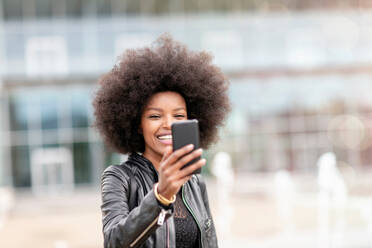 Young woman with afro hair taking smartphone selfie on city concourse - CUF51461